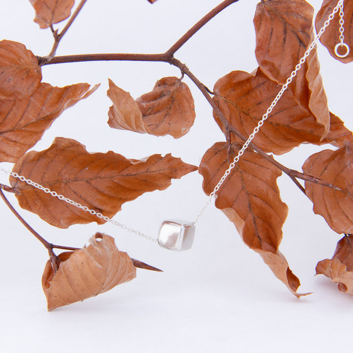 Sterling silver cube, dangles from branch of curled ridged russet leaves 