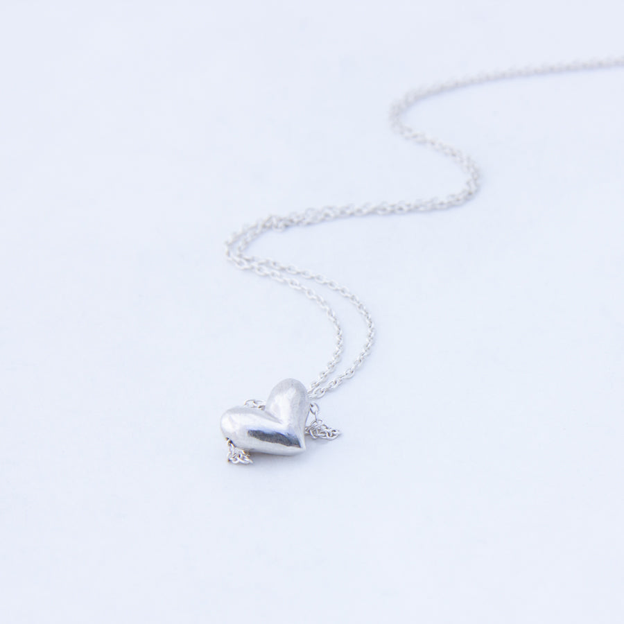 Close up view of carved silver heart necklace, chain in wave behind