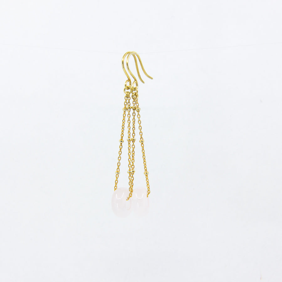 Pink gemstone and gold-plated chain earrings on white background