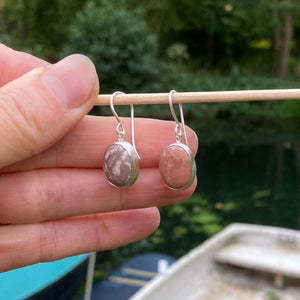 Dangle earrings from Found by You collection, held over bow of boat with river in background