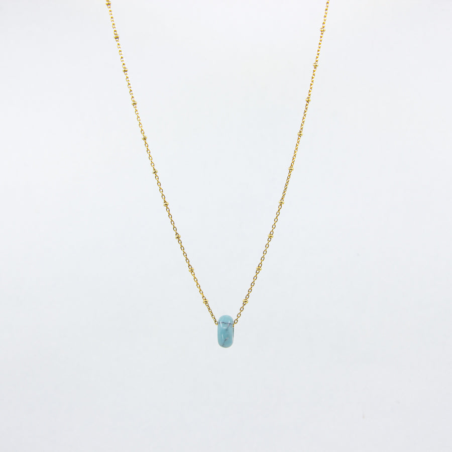 Turquoise gemstone and gold-plated necklace on white background