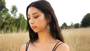 Woman wearing handmade silver and bead earrings in field of long yellow grass