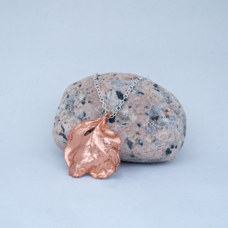 Back of medium copper leaf pendant, resting against speckled beach stone