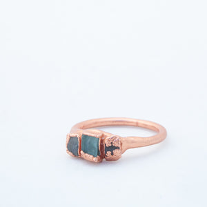 Ring from one side, showing the more encased smaller piece of glass to one side, on white background; and the other smaller piece to the right with copper surrounding all sides except the very bottom corner closer to the main piece of rectangle glass, which sits in the middle