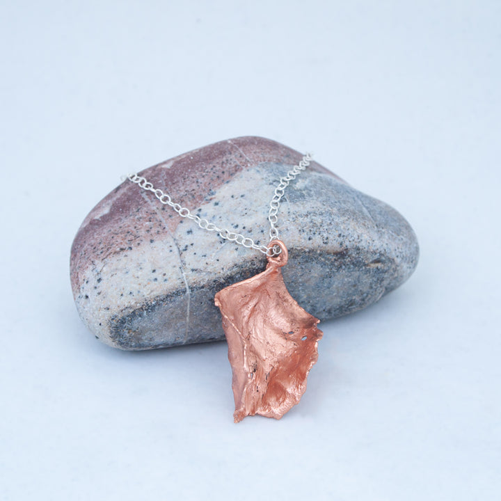 Leaf electroformed in copper, curling around on itself, resting against a red, white and grey striped beach stone