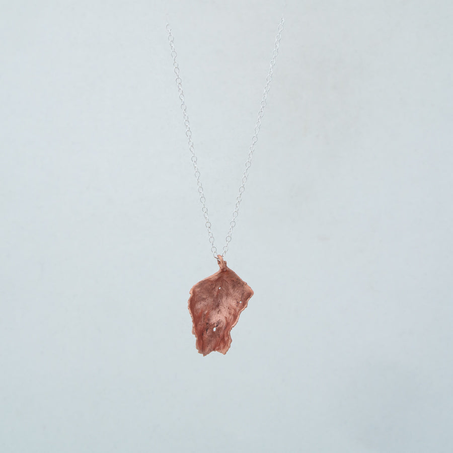 Curling copper leaf from front, dangling from silver chain against white background