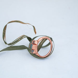 Sideways view of upcycled ring featuring broken windscreen glass, sitting within twirl and circles of dried green grass