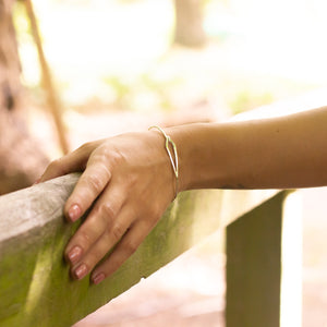 Close up of kite-shaped silver bangle on woman's wrist, her hand on wooden rail of a bridge