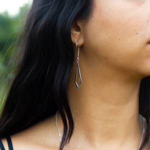 Side shot of handmade silver earrings in Dancing Kite design, in model's ear with her dark hair falling to the side
