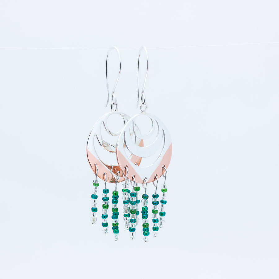 Close up of Spindrift earrings with silver topside and copper underneath, green blue and clear beads dangling beneath