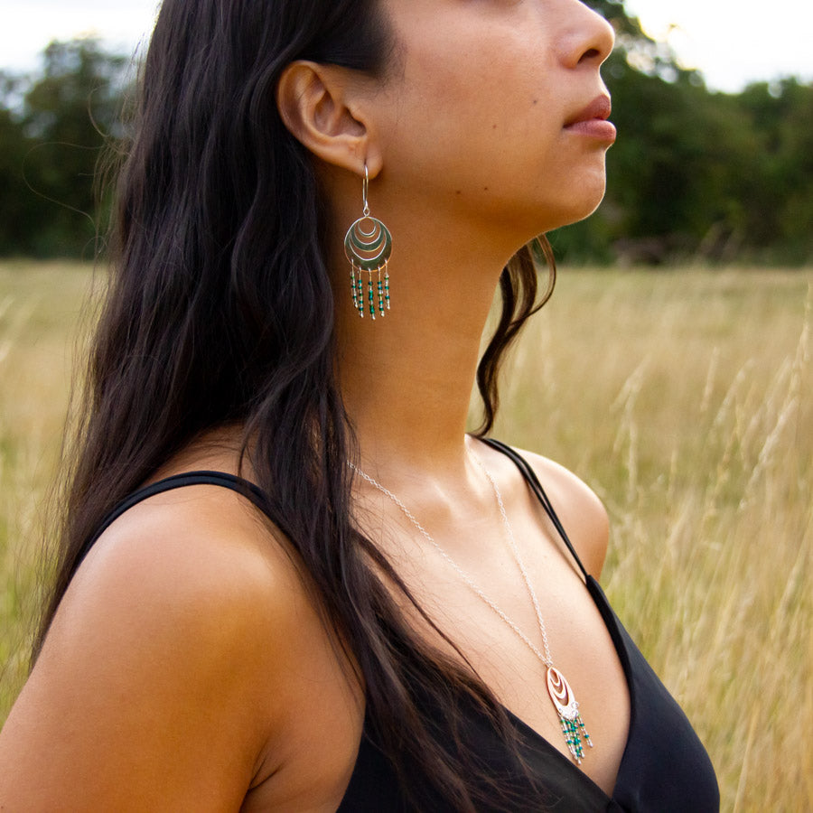 Neck and shoulder of model wearing unique handmade earring and necklace set in Spindrift design, with green-yellow grass behind