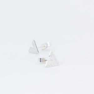 Emery paper version of sterling silver Slipstream studs, one in front of the other on white background