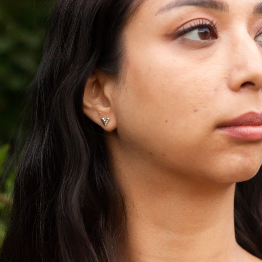 Close up of handmade small stud silver earring on model, green tree leaves behind, Slipstream design 