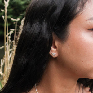 V-shaped handmade silver earring stud with texture, worn by model with long yellow grass and tree leaves behind