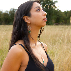 Model wears Spindrift handmade earrings and necklace set, looking up so face is in profile, in field of autumn grass