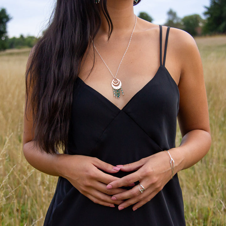 Spindrift necklace paired with Tailwind ring and Dancing Kite bangle and worn by model in black dress in field of grass