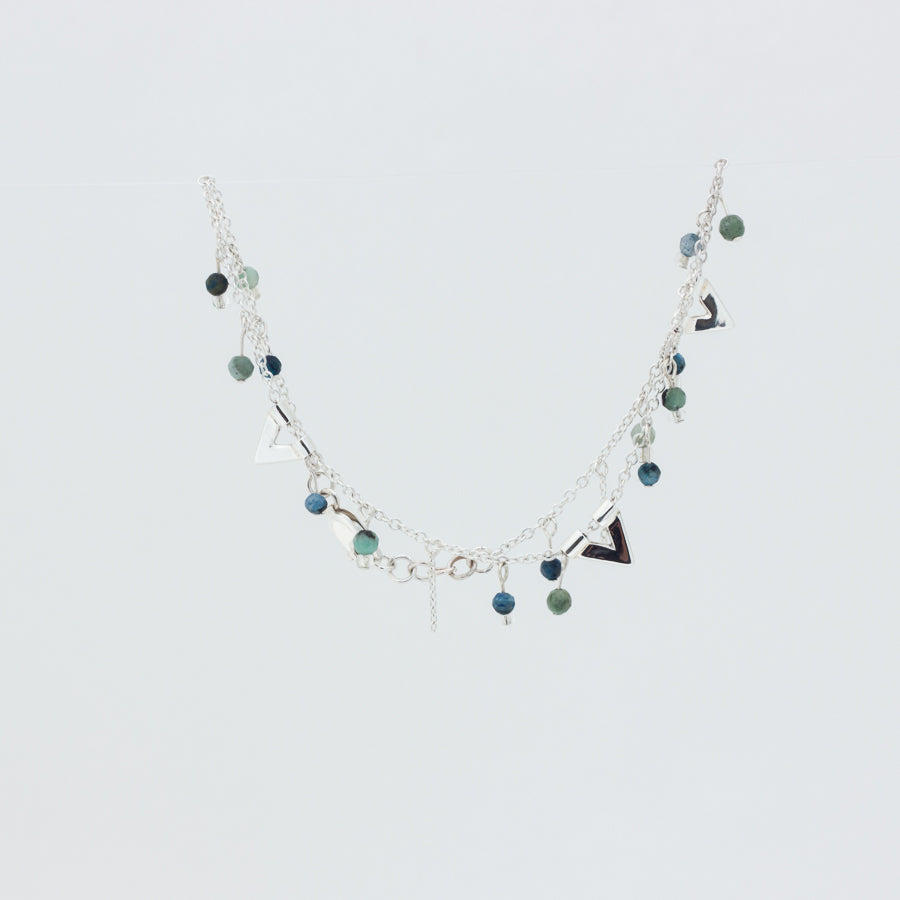 Close up of pretty silver anklet with green and blue beads, on white background