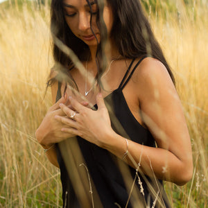 Model wearing full set of handmade silver jewellery including Tailwind ring and bracelet, Zephyr necklace and Dancing Kite bangle, looks down in praying post, in field of long yellowish grass