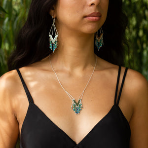 Model wears the Windcharm earrings and necklace with V-necked black dress and willow tree leaves behind