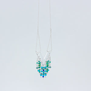 Slightly sideways view of Windcharm necklace on white background showing how chain threads through tube on top of pendant, and the colourful beads below