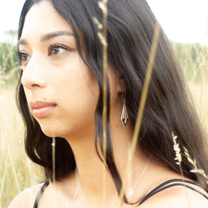 Model wearing Zephyr earrings amongst tall long yellow blades of grass
