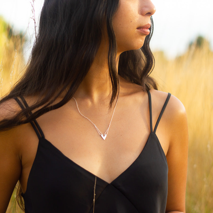 Unique handmade silver necklace worn by model who looks sideways in field of golden grass